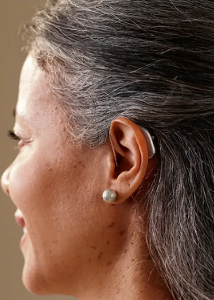 Mano ajustando audífono retroarticular detrás de la oreja